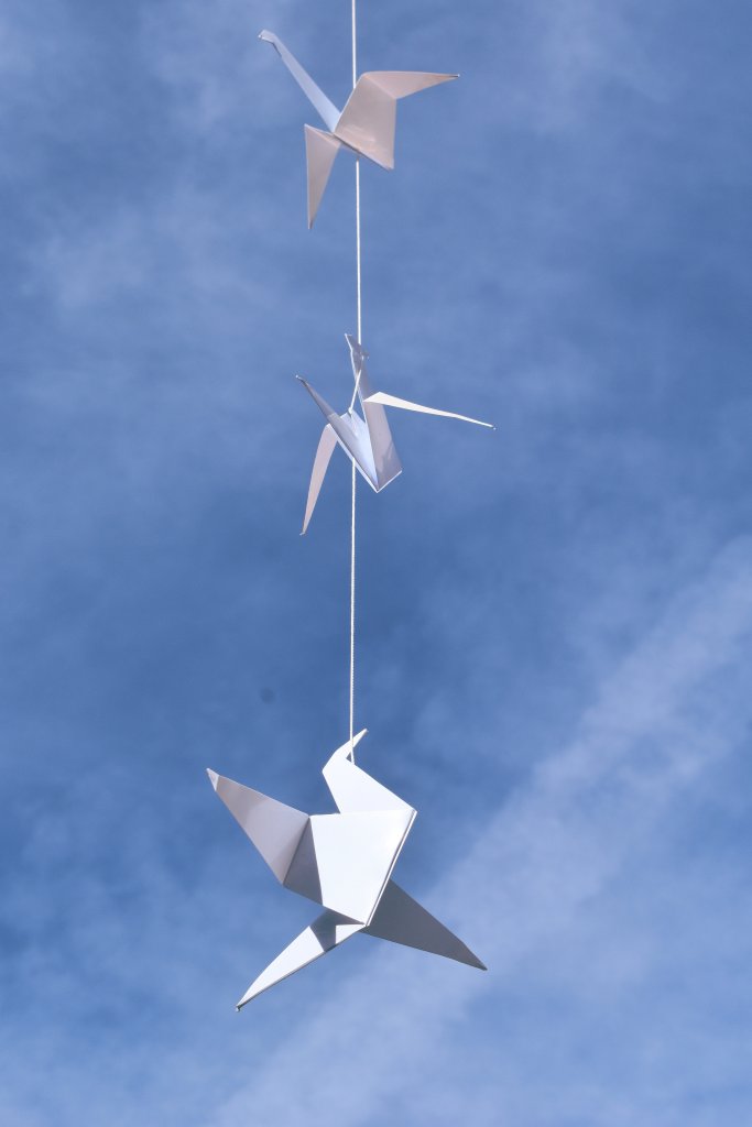 paper origami peace cranes hanging on a string with the blue sky behind them